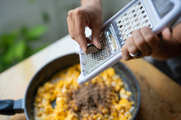 Middle age healthy eating. Woman in her kitchen grates a black truffle on an omelette, hands close-up.