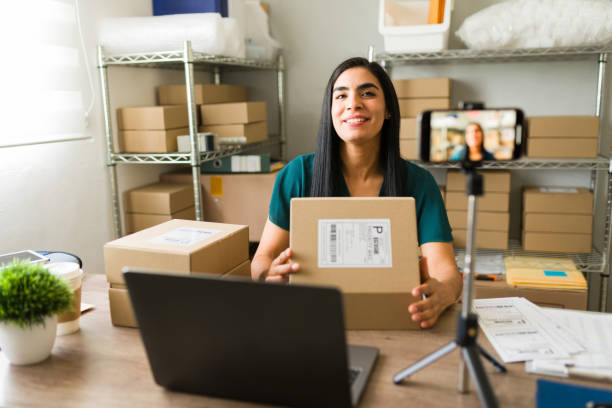 istock Beautiful woman holding a package while recording a video for her e-commerce business using a smartphone on a tripod 2187370259