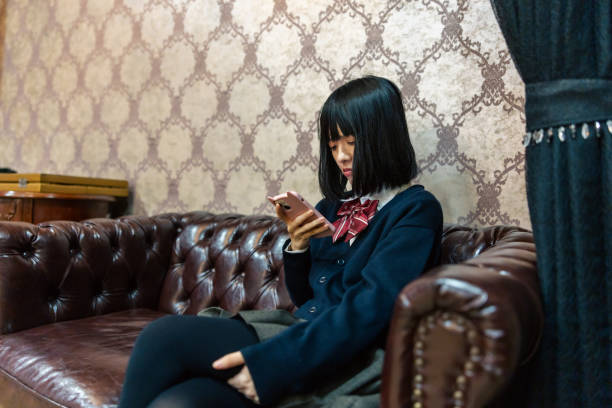 istock Woman in school uniform using smart phone in living room, sitting on sofa 2187384704