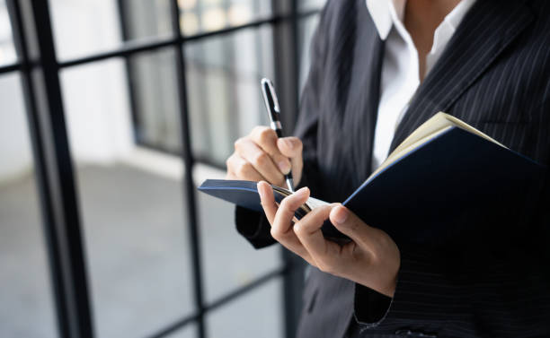 istock Business woman working from office taking reading and writing notes in note pad working on laptop computerÂ Â in her workstation. 2187391951