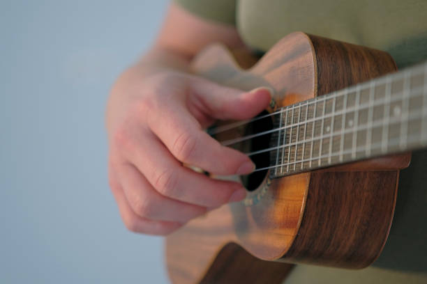 istock A man plays a ukulele, focus on the hand and strings, close-up. The ukulele is small and brown. A musician in a green T-shirt composes music on a ukulele 2187392236