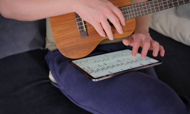 istock A man with a ukulele in his hands is looking through the notes of a new melody on a tablet. A guitarist learns to play the ukulele. The musician is sitting on the couch 2187392766