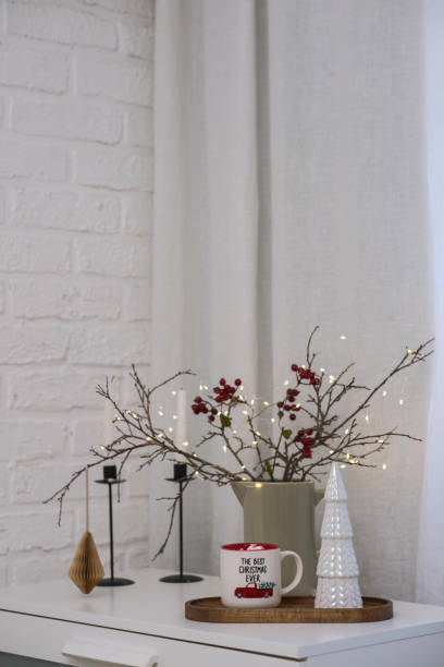 istock Hot cacao with marshmellows with Christmas dry tree branches with blurred lights and red berries, christmas tree on table in living room. 2187393042