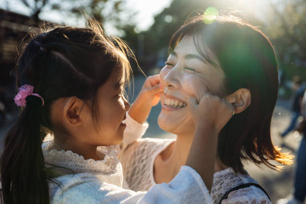 Daughter pulling cheeks of her laughing mother in tokyo park