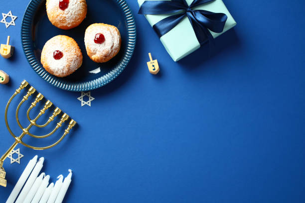 istock Hanukkah celebration flat lay with menorah, sufganiyot, dreidels, and gift box on blue background. 2187395733