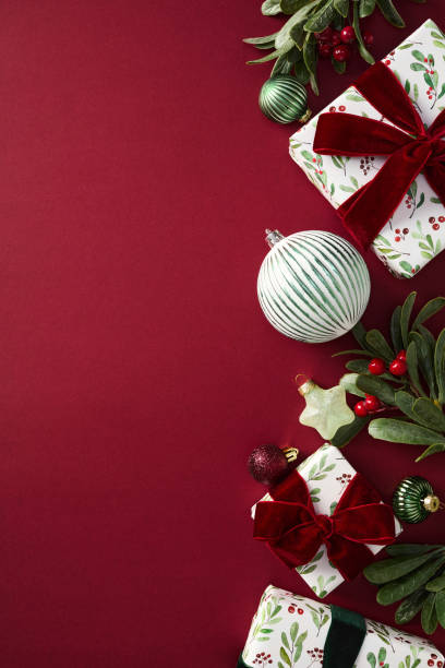 istock Stylish Christmas vertical background with gift box, balls, Xmas decorations, branches with berries on red table. Elegant, chic style. 2187395879