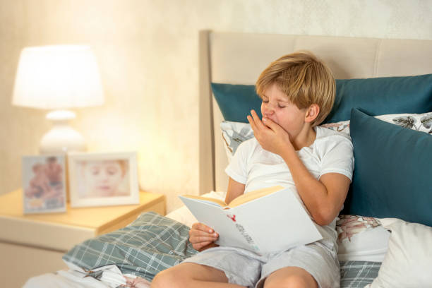 istock Teenage boy reading a book and yawning while lying on a bed 2187397852