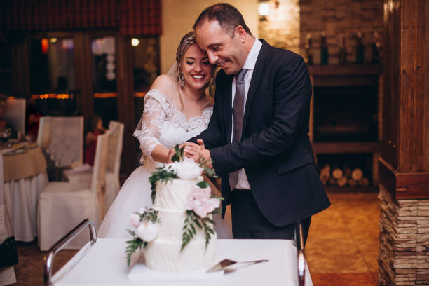 istock Newlyweds is cutting their wedding cake. beautiful cake. nicel light. wedding concept. Gorgeous bride and groom cutting a small modern wedding cake on a table with various decorations 2187405698