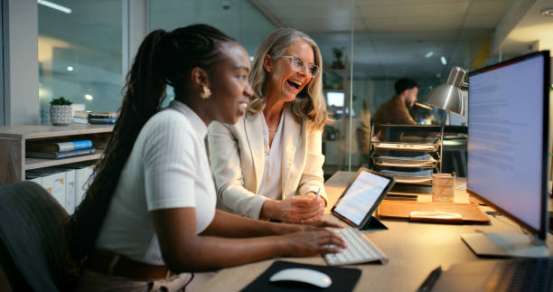 istock People, happy and computer in office for review, project proposal and collaboration at night. Women, reading and monitor screen in agency for email feedback, business pitch and pleased with deadline 2187408436