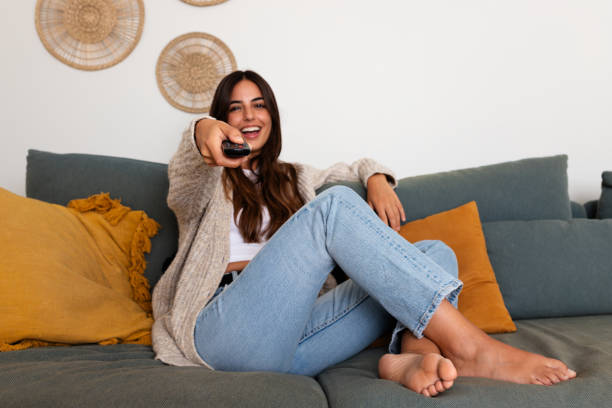 istock Young woman sitting on sofa watching tv and holding remote control 2187408484