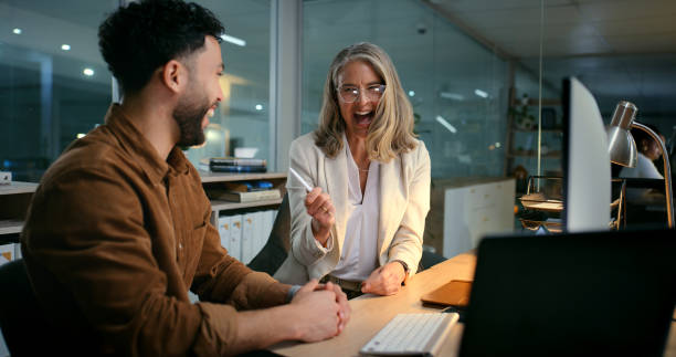 istock Collaboration, design and laughing with business people in office at night for web development. Computer, conversation or funny with mentor and employee in creative workplace for project deadline 2187408539
