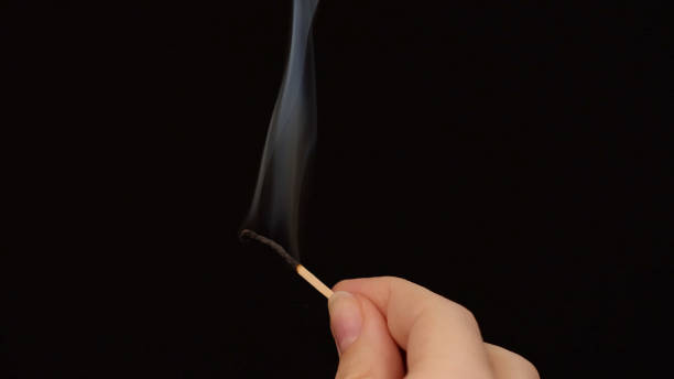 istock hand holding a burnt matchstick with smoke trailing upwards, against a black background 2187408641