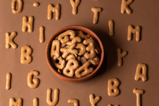 A collection of alphabet-shaped cookies artfully arranged in a bowl and scattered across a brown surface, perfect for creative culinary presentations or educational concepts.