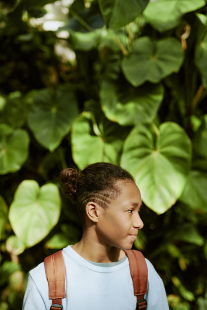 istock Teen Boy Looking Away While Standing Against Green Plants 2187414489