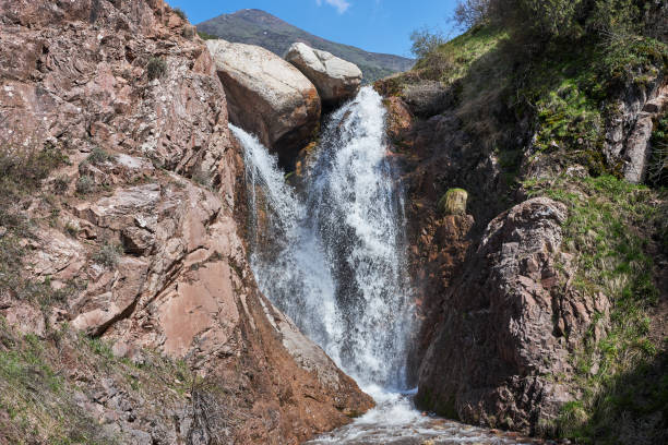 Waterfall in mountains area, rocky cliff. Two streams join into one. Summer natural landscape. Travel destination in Kyrgyzstan.