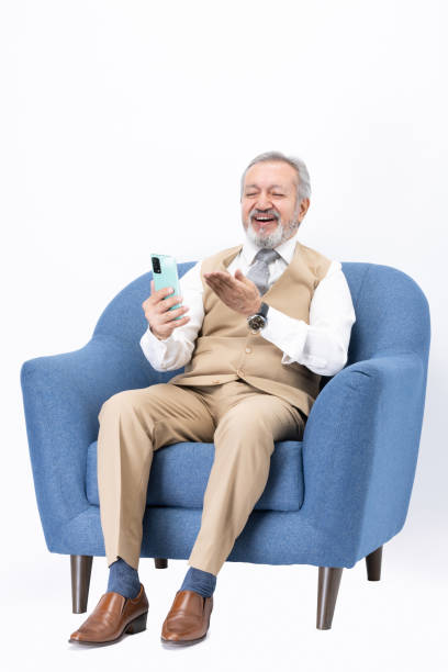 istock Senior man using phone sitting on sofa isolated white background stock photo 2187423228
