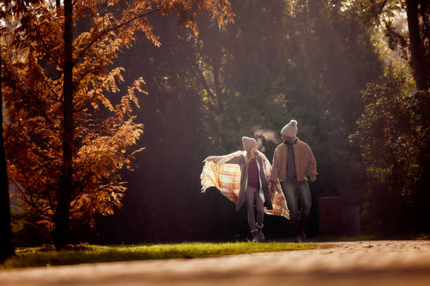 Happy diverse couple having fun while holding hands during their walk in autumn day at the park.