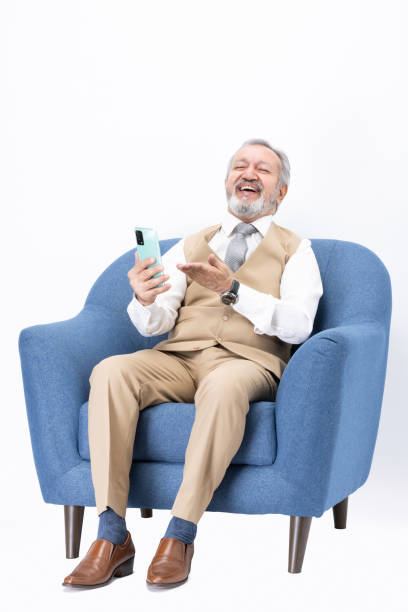 istock Senior man using phone sitting on sofa isolated white background stock photo 2187423316