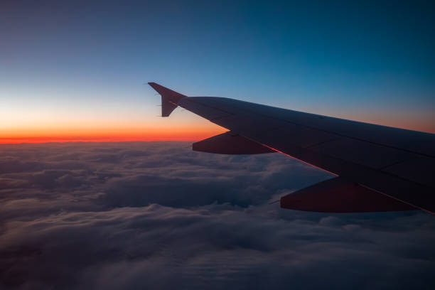 An airplane wing over a blanket of clouds, with a gradient sunset or sunrise