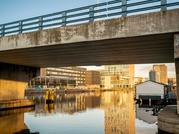Amsterdam, Netherlands - Nov 29, 2019: Buildings bathe in golden sunlight viewed through the De Heusweg overpass bridge. Along the Duivenrechtsevaart (river).