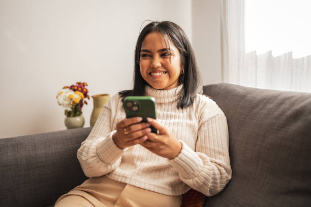 istock Smiling woman sitting on a couch using a smartphone at home 2187441815