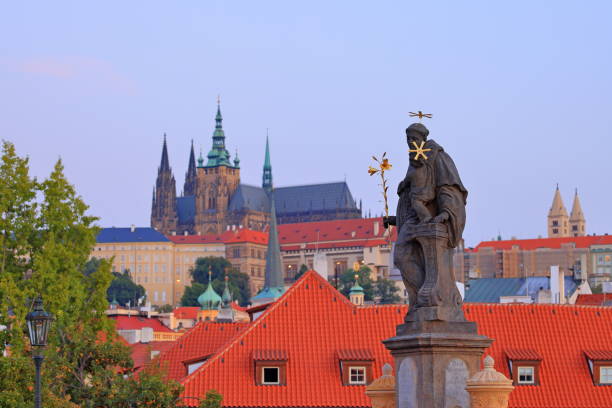 Scenic view from Charles Bridge in Prague, featuring historic statues, gothic architecture, and Prague Castle in the background at sunset.