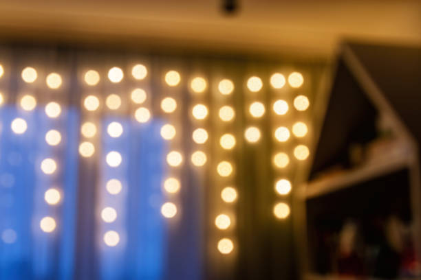 Blurred image of warm, inviting bokeh lights strung across a curtain, creating festive ambiance. Festive cozy room interior