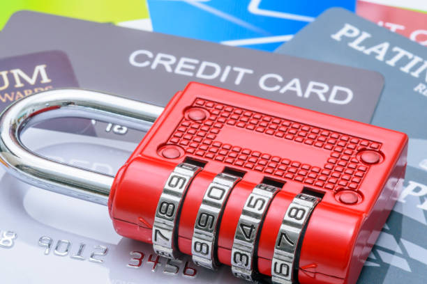 Financial or credit card security, identity theft prevention, and data protection : A red combination padlock placed over multiple credit cards, depicting themes of cybersecurity, fraud protection.