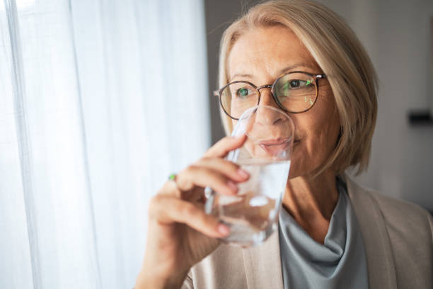 istock Senior woman in glasses drinking water by a window 2187449239