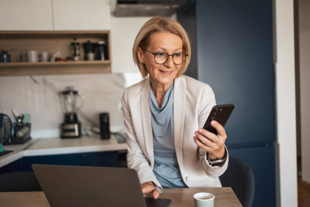 istock Smiling mature woman using smartphone at home office desk 2187449241