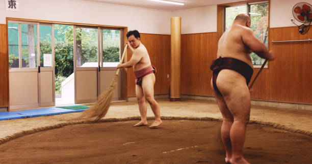 istock Ceremony, broom and dohyo with Sumo wrestler people sweeping sand in mawashi, getting ready for competition. Cleaning, prepare and start with men in Japan for culture, heritage or martial arts 2187452416