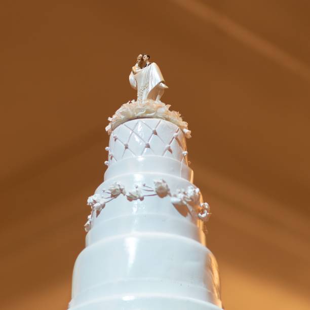 Elegant white wedding cake with a bride and groom topper, adorned with floral decorations, under warm lighting.