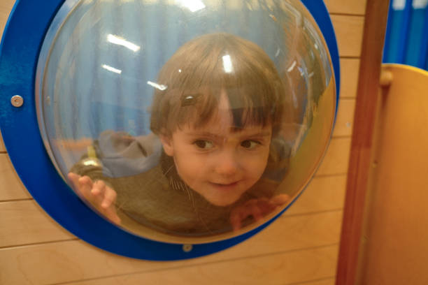 Curious baby boy peering through a plastic bubble window in a playground, enjoying a playful game of hide and seek