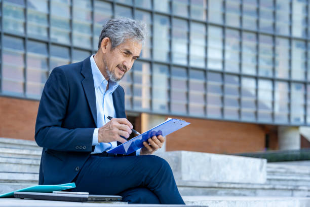 istock old experienced businessman in suit casual working during break,sitting and writing on documents outdoors the building 2187462739