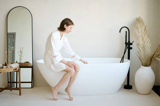 istock Young Woman Dressed in Bathrobe Sitting on Bathtub 2187463358