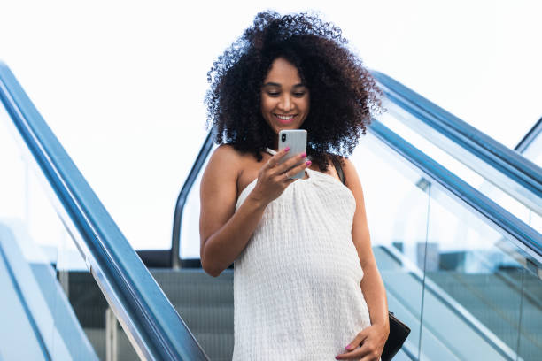 istock Pregnant black woman browsing smartphone on escalator 2187463414