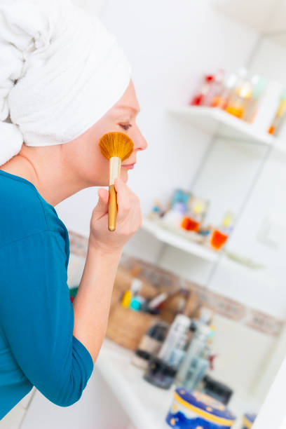 Mature woman applying make-up with a make-up brush in front of a mirror in her bathroom.