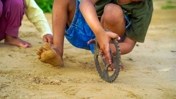 A young child playing with his toys on the sand ground. Asian kid is rolling the spinning wheel on soil. kids activities in outdoor.