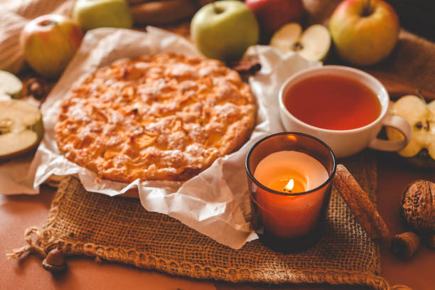 istock A cozy autumn setup featuring a freshly baked apple pie surrounded by apples, walnuts, a candle, and a warm drink 2187472108