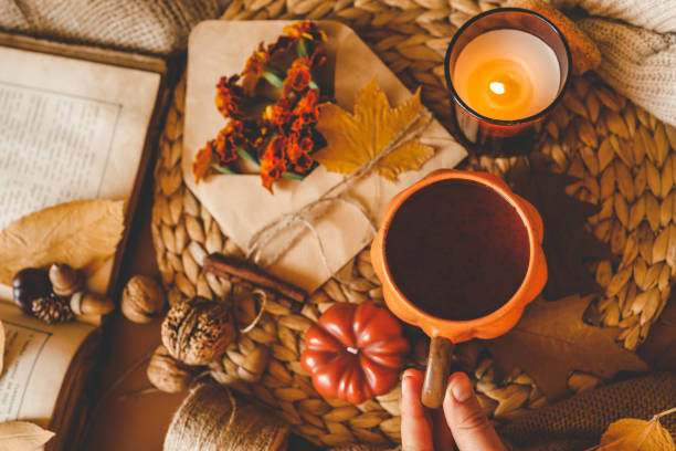 istock Cozy flat lay composition featuring an orange pumpkin-shaped mug of hot drink, a lit candle, marigold flowers, and autumn leaves on a woven surface, creating a warm and rustic autumnal mood 2187472459