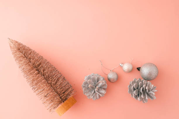 Minimalist flat lay composition of a metallic Christmas tree, silver pinecones, and glittery ornaments on a pastel pink background. Perfect for festive, seasonal, and holiday-themed designs
