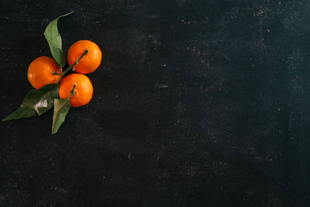 Fresh tangerines with green leaves arranged on a textured dark background. Minimalist composition highlighting vibrant citrus colors, ideal for seasonal, food, or natural-themed visuals