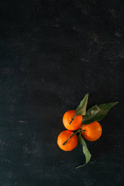 istock Fresh tangerines with green leaves arranged on a textured dark background. Minimalist composition highlighting vibrant citrus colors, ideal for seasonal, food, or natural-themed visuals 2187475850
