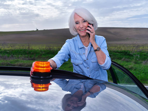 Elderly woman with her broken down car puts the emergency light on the roof while calling her insurance company to have the tow truck come