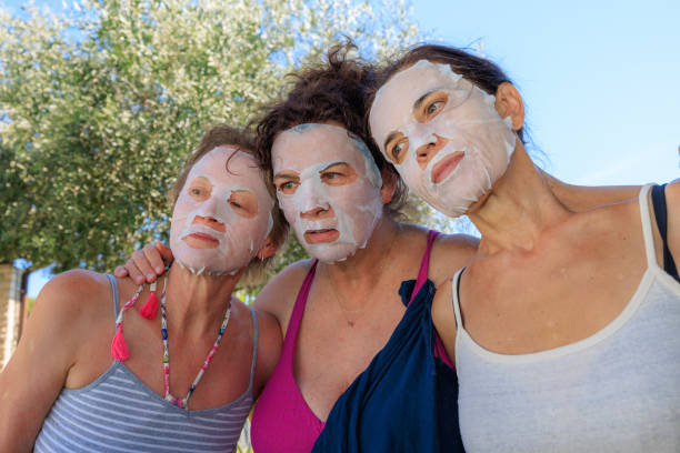 Portrait of three women outdoors with collagen mask on their faces against flowering olive tree.
