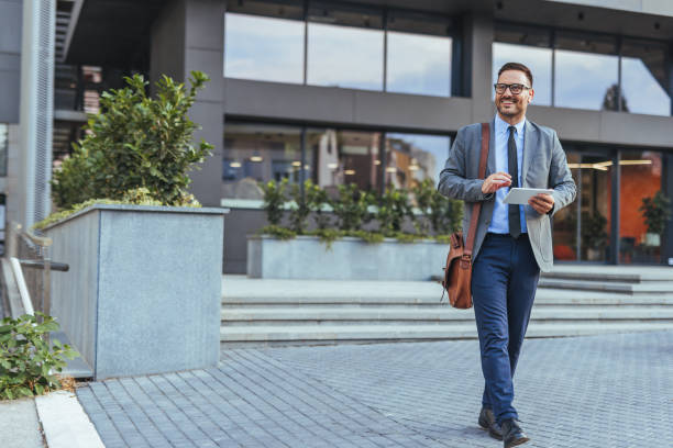 istock Confident Businessman Walking Outside Modern Office Building With Tablet 2187502489