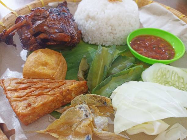 istock Grilled duck on a traditional plate on a wooden background. Flat lay. Selective focus. Traditional Indonesian menu, grilled chicken with tofu, tempeh, chili sauce and fresh vegetables. 2187518387