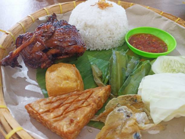 istock Grilled duck on a traditional plate on a wooden background. Flat lay. Selective focus. Traditional Indonesian menu, grilled chicken with tofu, tempeh, chili sauce and fresh vegetables. 2187518424
