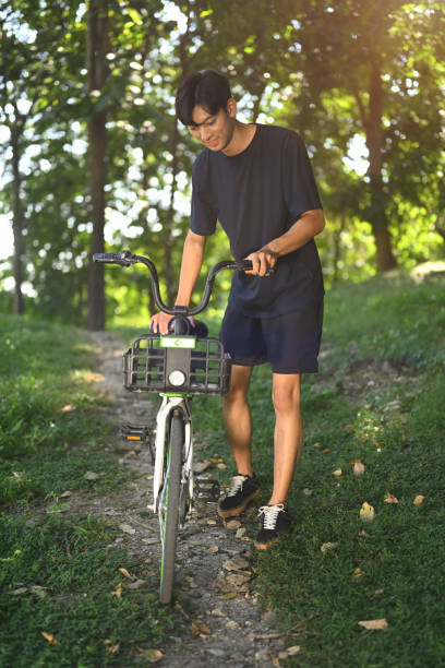 istock Young asian man pushing his bicycle walking through forest path on a beautiful sunny day 2187531232