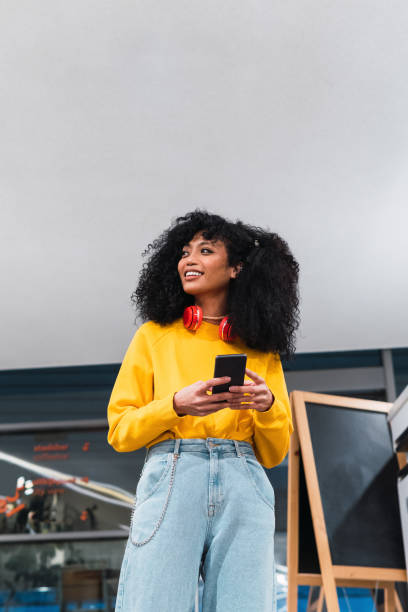 istock Cheerful stylish ethnic lady standing and using smartphone in contemporary building 2187531424